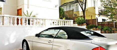 A white convertible car parked in front of a building with a white fence and a balcony.