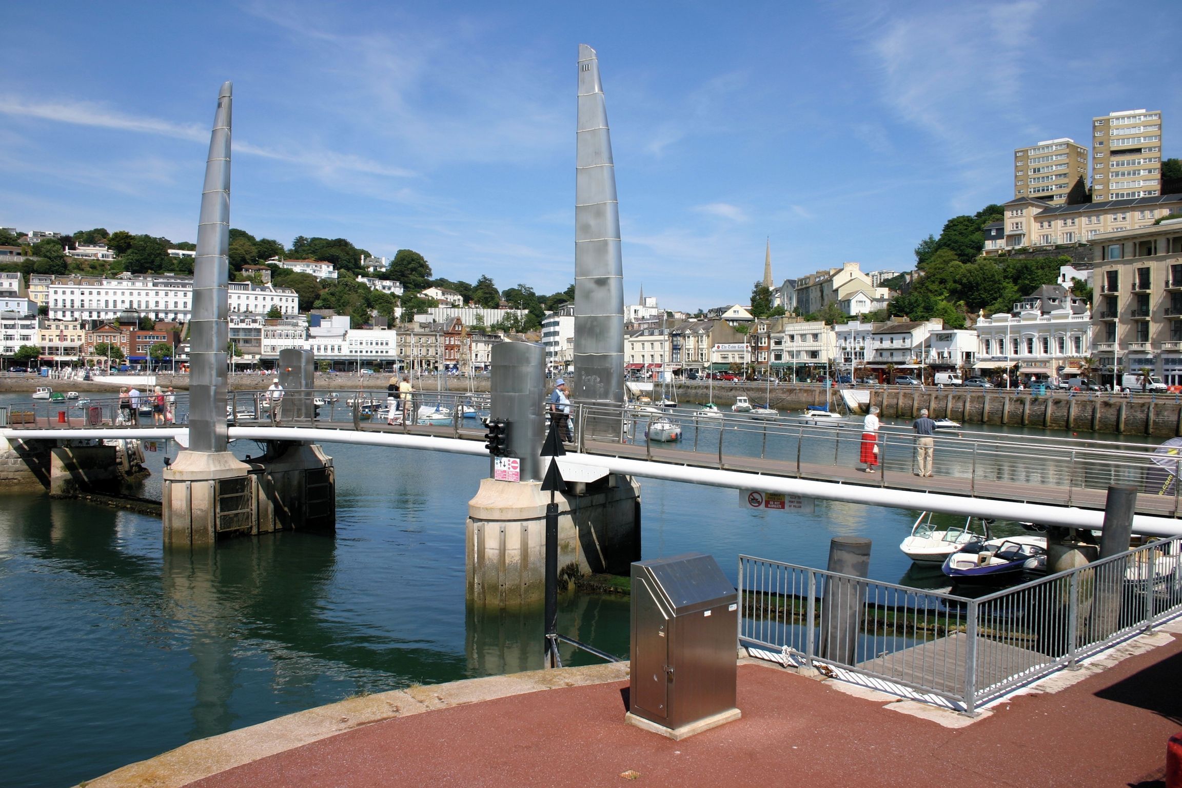 A waterfront promenade with a bridge, boats, and buildings in the background.