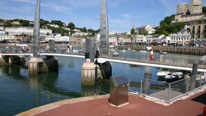 A waterfront promenade with a bridge, boats, and buildings in the background. - The Baytree (Torquay)