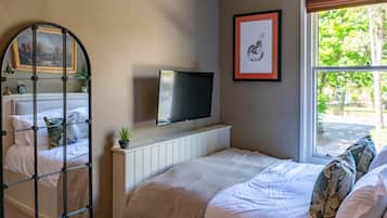 Un dormitorio con cama, televisor montado en la pared, ventana con vistas a árboles y un cuadro enmarcado en la pared.