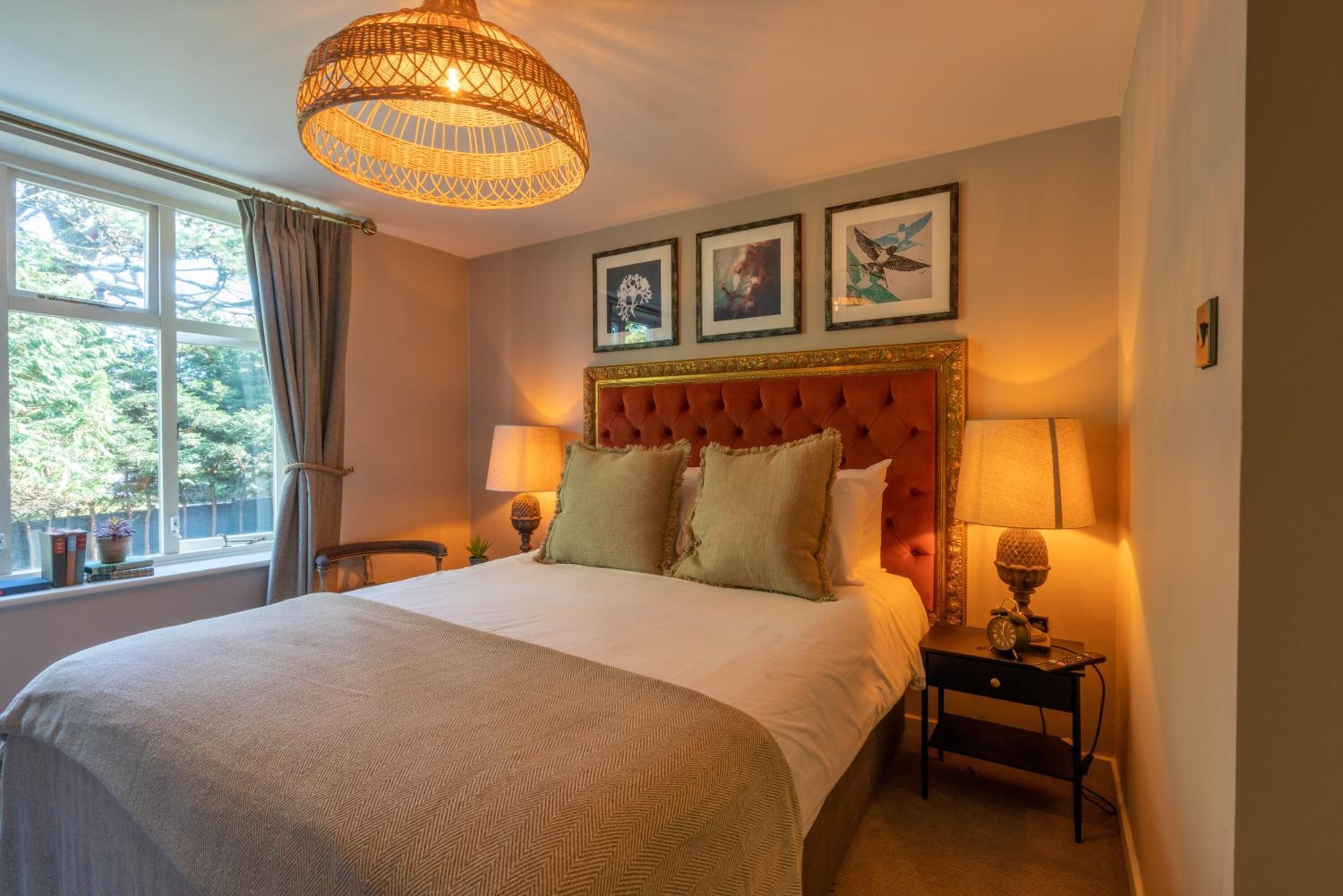 A neatly made bed with a red headboard, two bedside lamps, and three framed pictures on the wall.