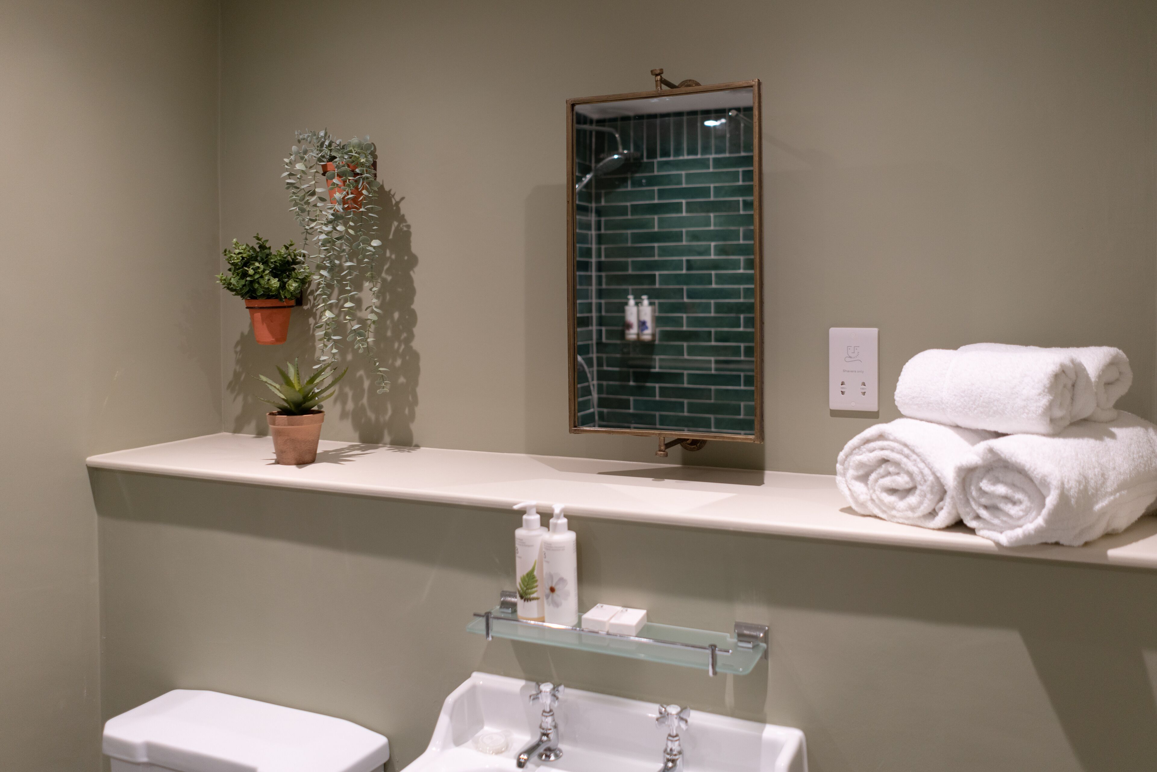 Un baño con inodoro blanco, repisa de vidrio con artículos de aseo, espejo y toallero con toallas dobladas.