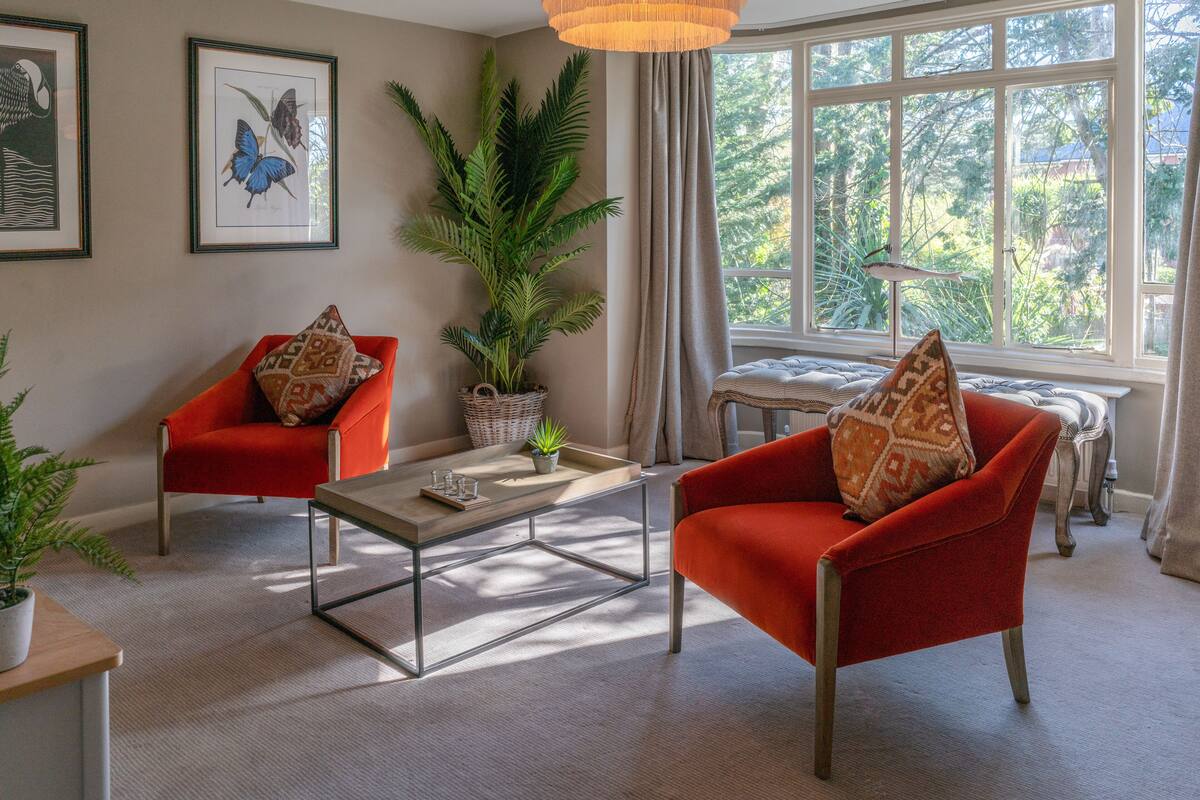A living room with two red armchairs, a coffee table, a large potted plant, and framed butterfly artwork on the wall.