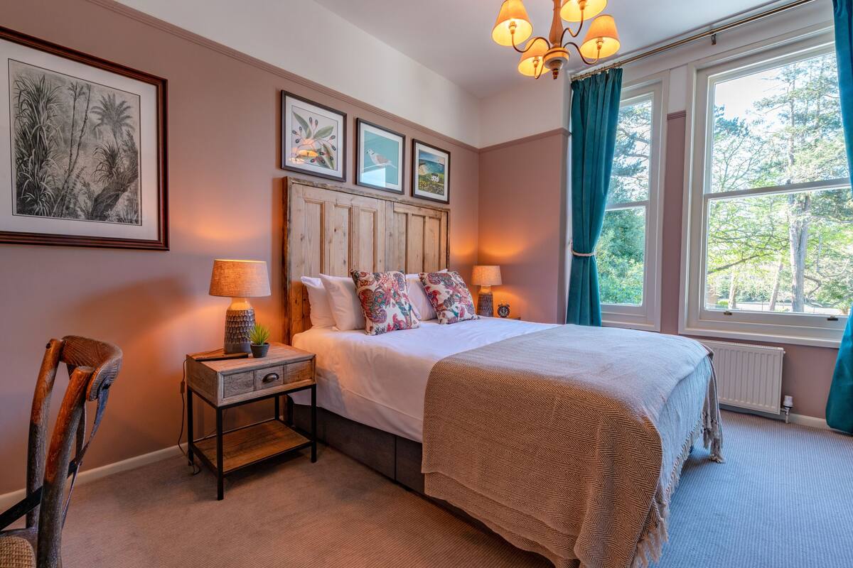 A bedroom with a wooden headboard, a large bed with patterned pillows, bedside lamps, and framed artwork on the wall.