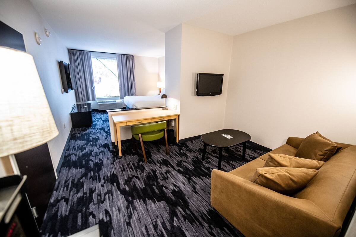 Une chambre d’hôtel comprenant un lit, un bureau, une chaise, un canapé, une télévision et un sol recouvert de moquette.