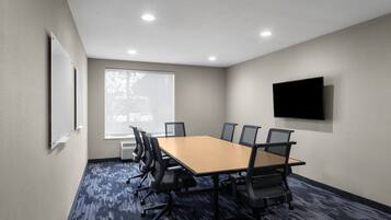 Uma sala de conferências com uma mesa grande, seis cadeiras, uma TV de tela plana e uma janela com persianas.