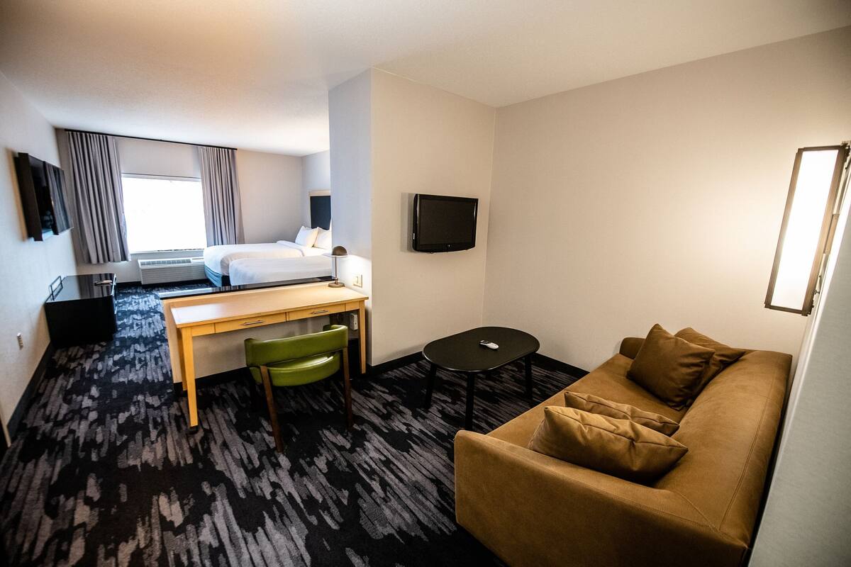 Une chambre d’hôtel avec un lit, un bureau, une chaise, une télévision et un canapé.
