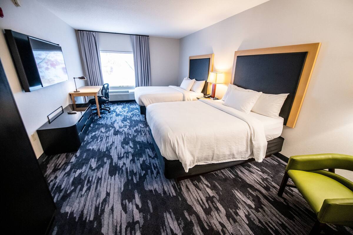 Une chambre d’hôtel avec deux lits, un bureau, une chaise et un téléviseur.
