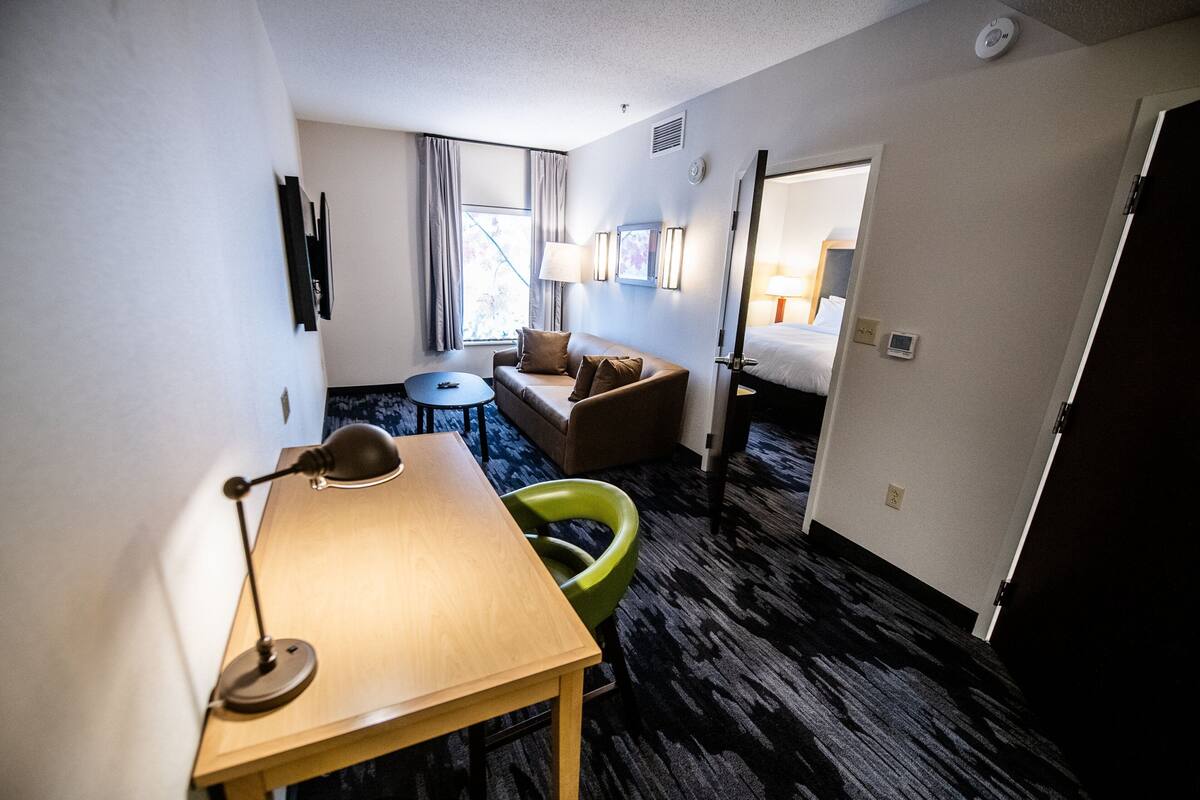 Une chambre d’hôtel avec un bureau en bois, une chaise verte, un canapé, une petite table et un lit.