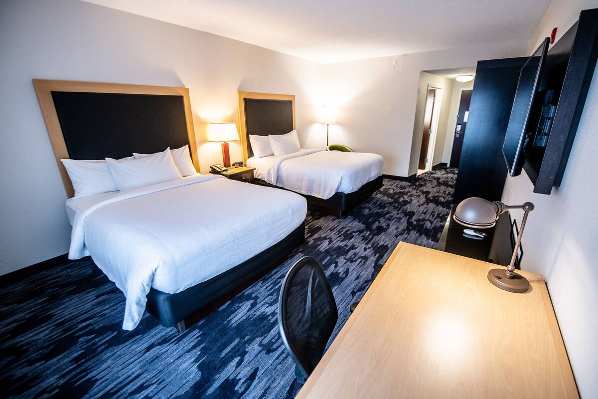Une chambre d’hôtel avec deux lits, un bureau, une chaise, une télévision et une lampe.