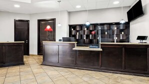 A reception area with a dark wood reception desk, a red lamp, and a modern light fixture. - SureStay Plus Hotel by Best Western Lubbock Medical Center (Lubbock)