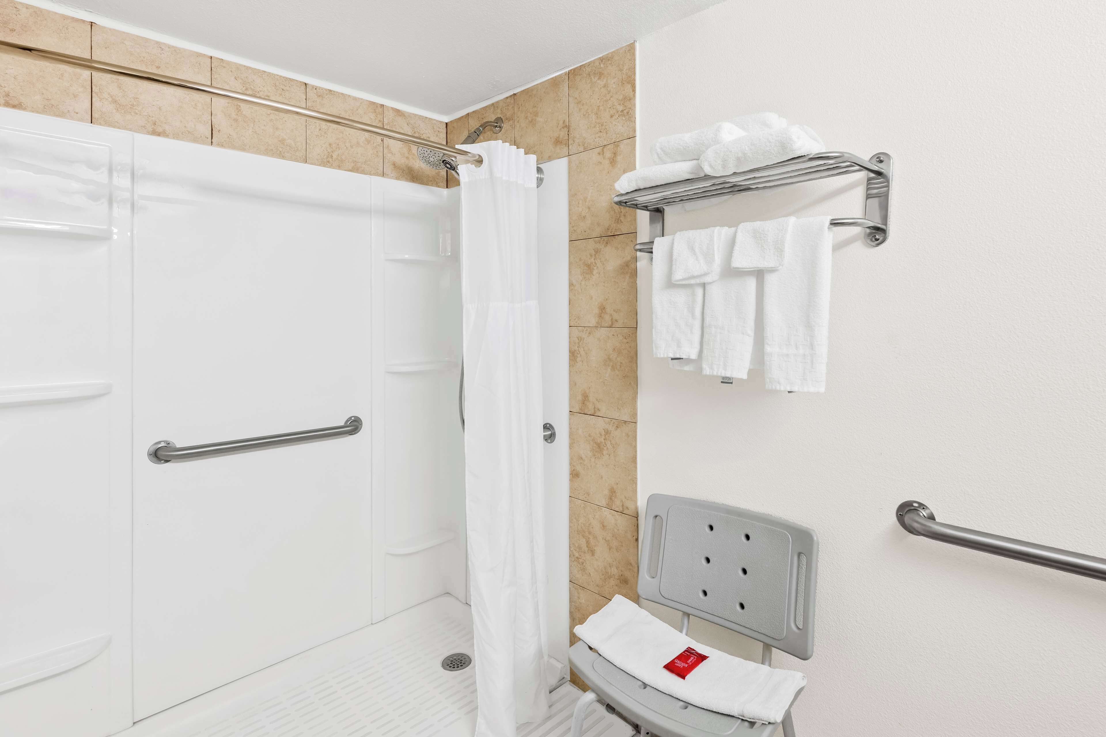 A bathroom with a shower, toilet, and handrails.