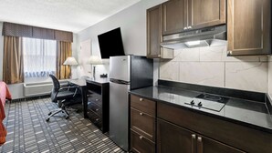 A compact hotel room with a kitchenette, a flat-screen TV mounted on the wall, a desk with a chair, and a window with curtains. - SureStay Plus Hotel by Best Western Lubbock Medical Center (Lubbock)