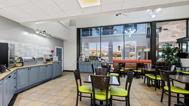 A modern restaurant with a kitchen area, dining tables with chairs, and large windows offering a view of the outside. - SureStay Plus Hotel by Best Western Lubbock Medical Center (Lubbock)