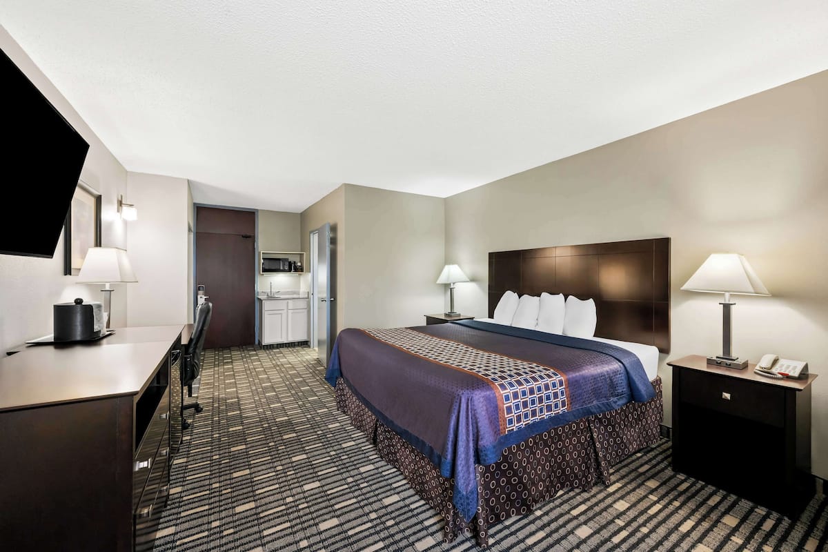 Une chambre d’hôtel comprenant un lit, un bureau et une table de chevet, avec un tapis à motifs et des murs aux couleurs neutres.