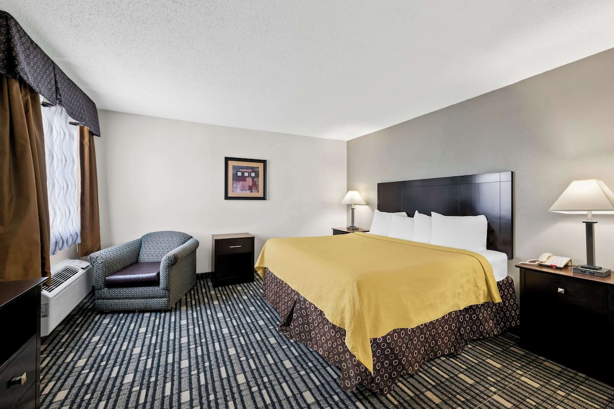 Une chambre d’hôtel avec un lit, une chaise, une table de chevet, une lampe et un tableau au mur.