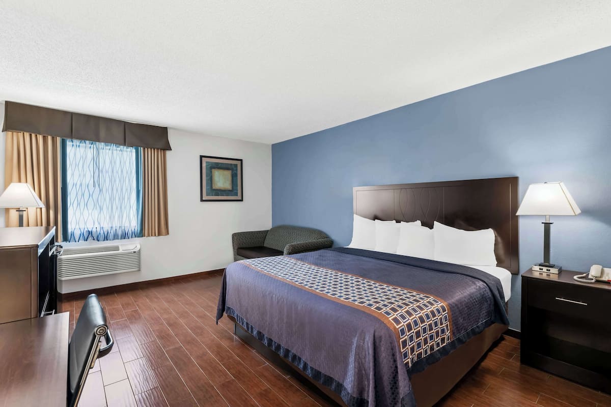 Une chambre d’hôtel avec un lit, une table de chevet, une lampe et une fenêtre avec des rideaux.