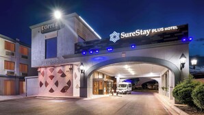 A hotel entrance with a 'SureStay Plus Hotel' sign, a 'Copper Lounge' sign, and a modern architectural design with a covered entrance and a van parked outside. - SureStay Plus Hotel by Best Western Lubbock Medical Center (Lubbock)