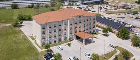 A multi-story hotel with a central courtyard, parking lot, and a nearby commercial building.