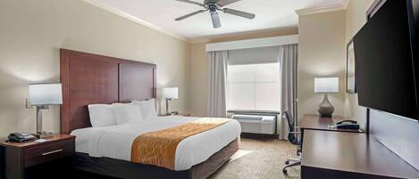 Ein Hotelzimmer mit einem Bett, einem Schreibtisch, einem Fernseher, einem Deckenventilator und einem fenster mit Vorhängen.