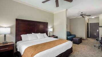 Una habitación de hotel con una cama grande, dos mesitas de noche, un escritorio, una silla y un ventilador de techo.