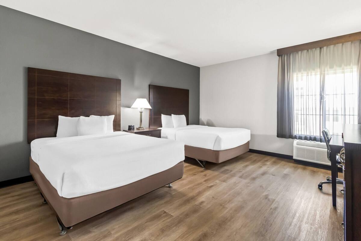 A hotel room with two beds, a desk, a lamp, and a window with curtains.