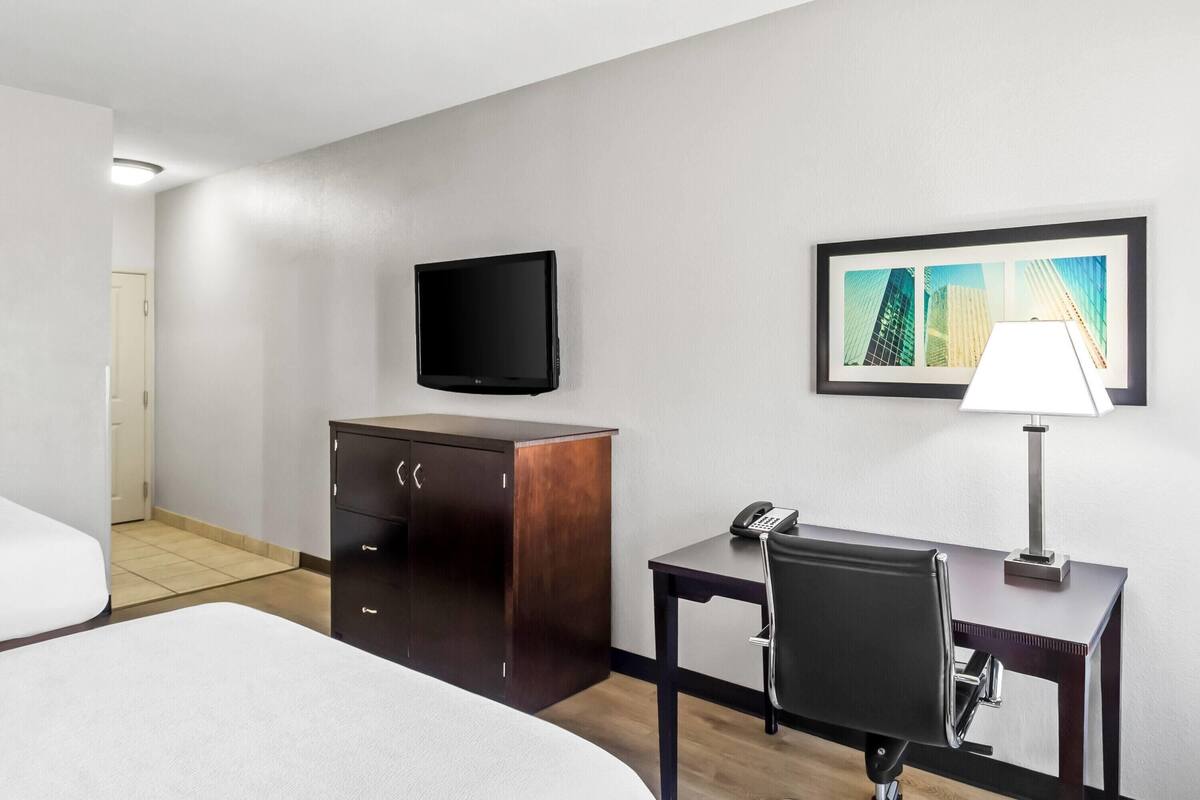 A hotel room with a bed, a desk with a chair, a telephone, a television, a cabinet, and a framed picture on the wall.