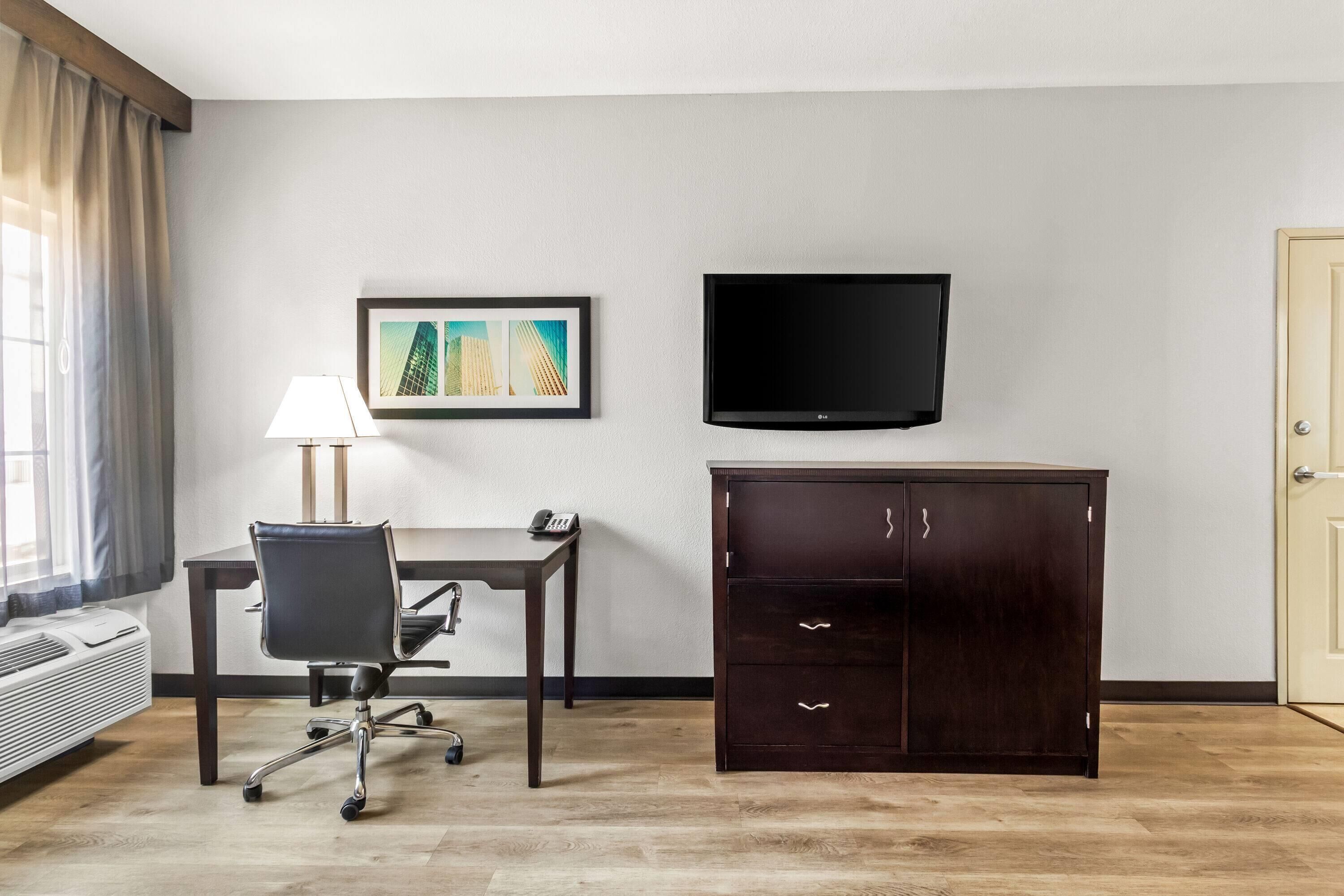 Habitación de hotel con escritorio, silla, televisor y armario.