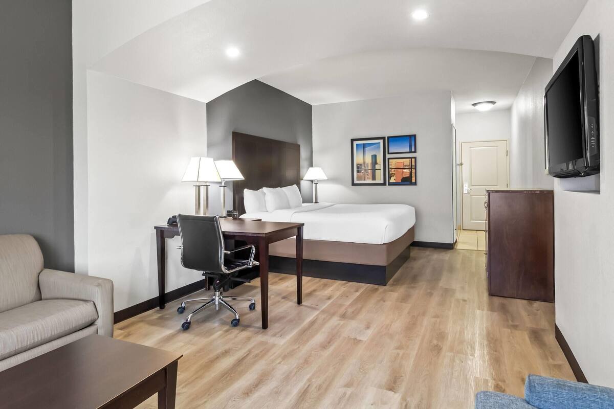 A hotel room with a bed, desk, chair, and a TV.