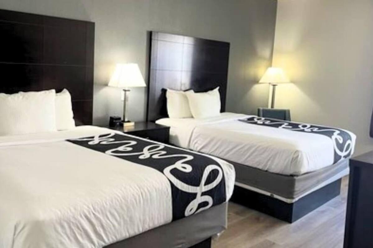A hotel room with two beds, each with a headboard and bedside tables.