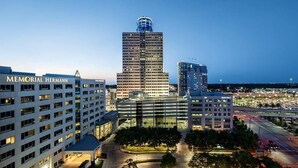 Eine Stadtansicht mit einem markanten Memorial Hermann Gebäude, einem hohen Wolkenkratzer und einem Parkplatz.
