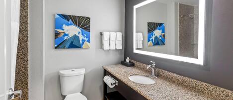 A modern bathroom with a toilet, sink, and large mirror. There are towels on the wall and a picture of a bridge.
