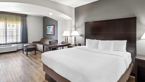 Ein Hotelzimmer mit einem großen Bett, einem Schreibtisch, einem Sessel, einer Couch und einem Vorhangfenster.