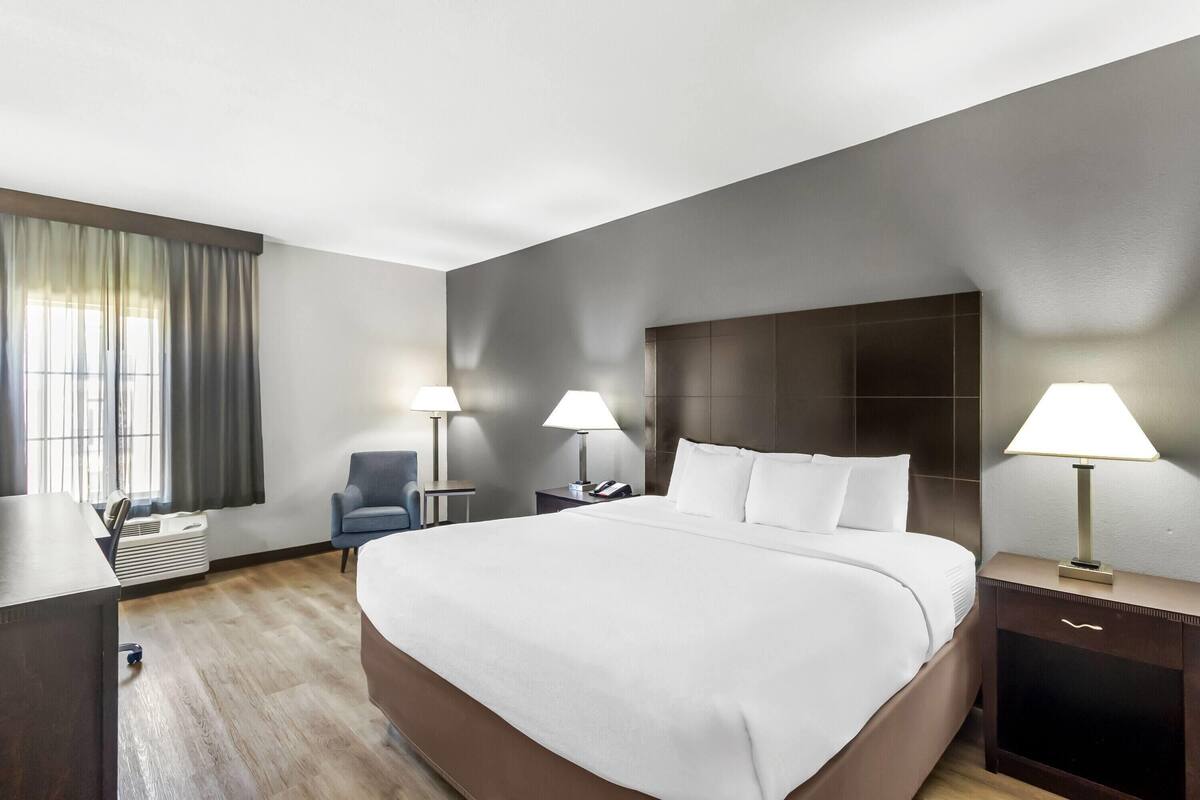 A hotel room with a large bed, two bedside tables with lamps, a desk, and a chair.