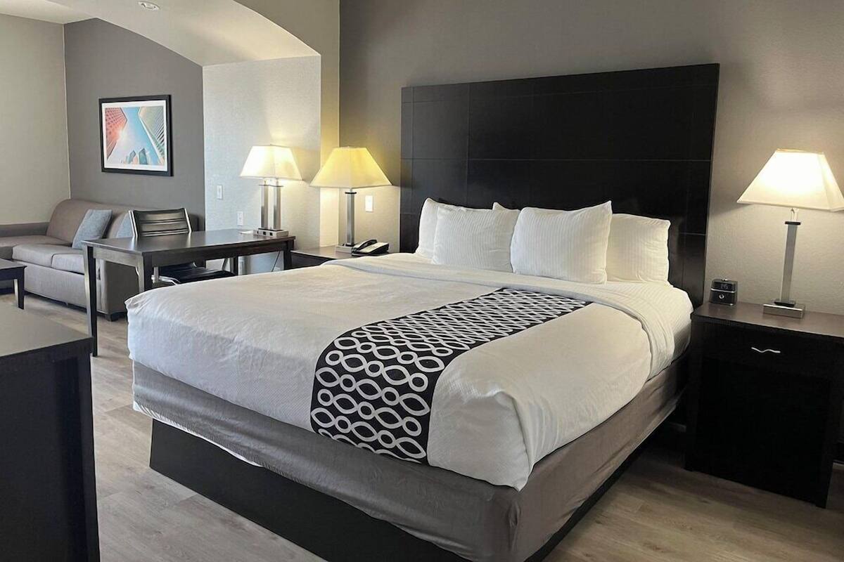 A hotel room with a large bed, bedside tables, a desk, and a sofa.