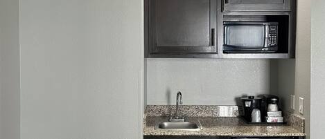 A compact kitchen with dark cabinets, a built-in microwave, a sink, and a coffee maker.