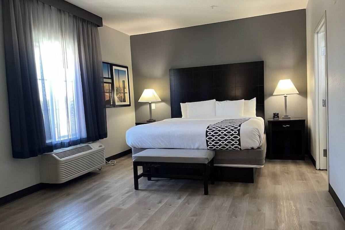 A hotel room with a bed, bedside tables, a heater, and a window with curtains.