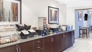 Zona de desayuno de hotel con barra libre, que incluye un expositor de vidrio, cestas de pan y una máquina de café.