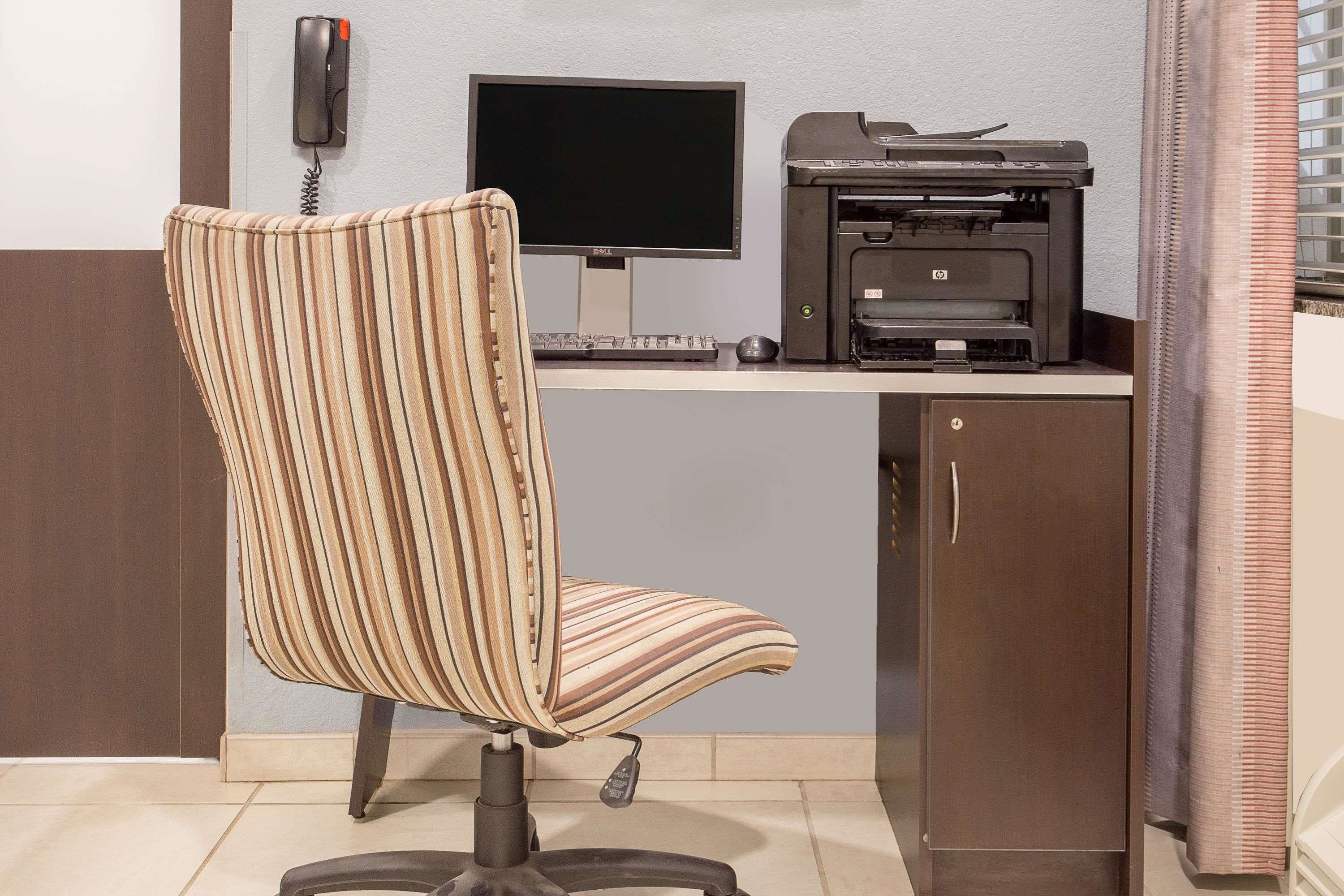 A workspace with a striped chair, a desk, a monitor, a printer, and a telephone.