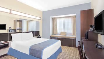 A hotel room with a large bed, a desk with a chair, a television, and a window with curtains.