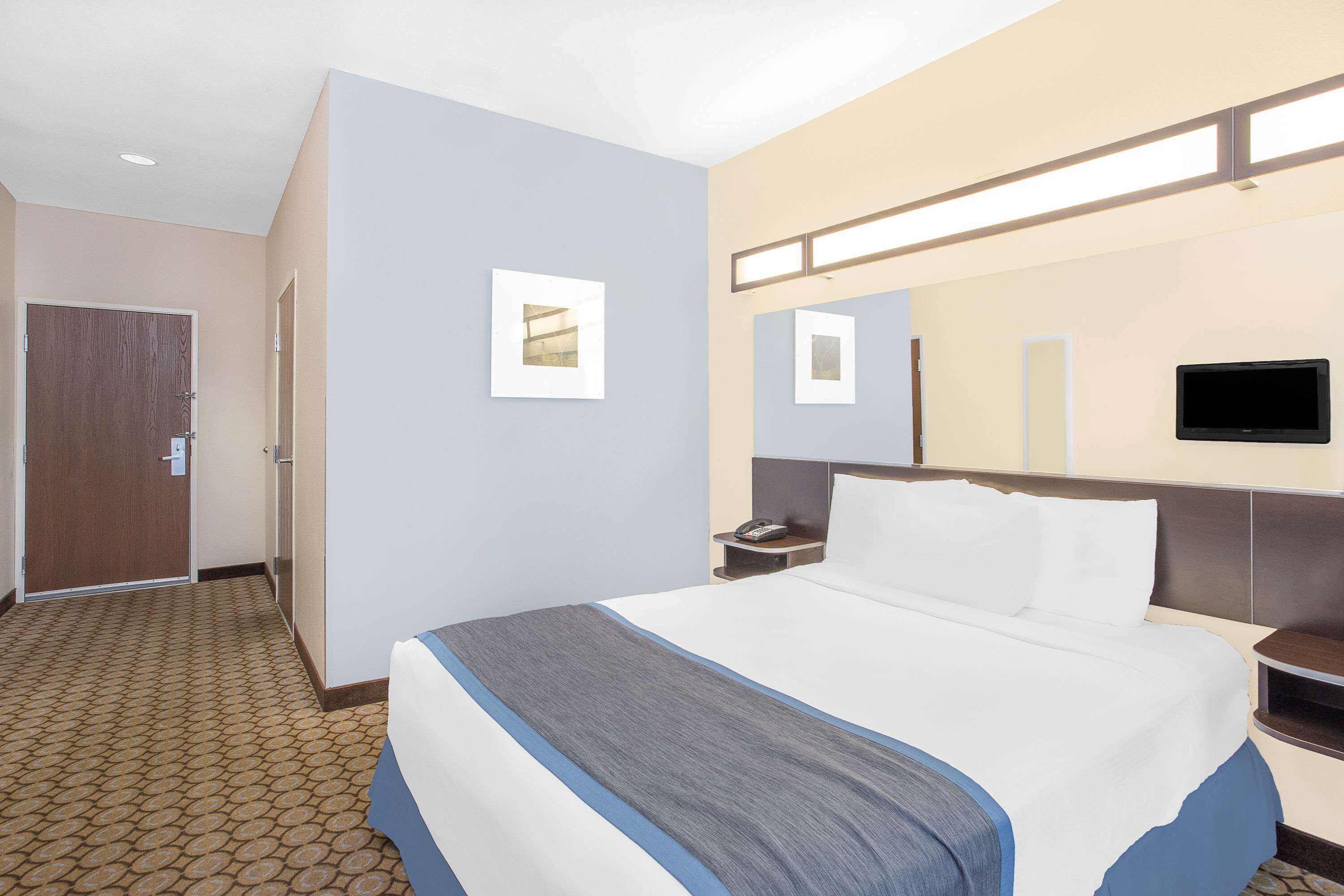 A hotel room with a bed, a nightstand, a TV, and a door.