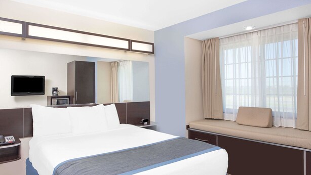 Habitación de hotel con una cama grande, una mesita de noche con teléfono, televisión, microondas y ventana con cortinas.