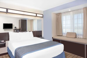 A hotel room with a large bed, a bedside table with a phone, a TV, a microwave, and a window with curtains. - Microtel Inn & Suites by Wyndham San Angelo (San Angelo)