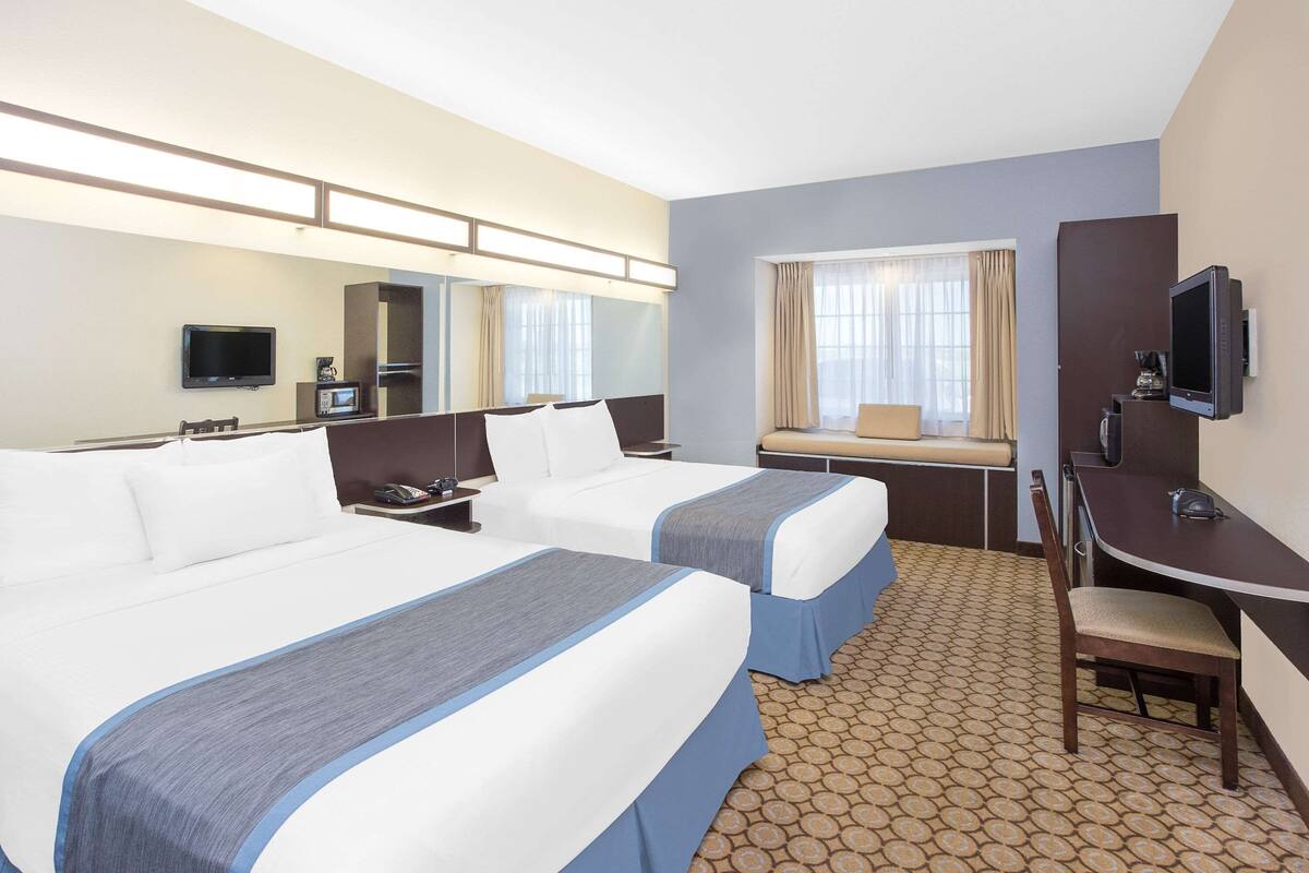 A hotel room with two beds, a desk, a chair, a television, and a window with curtains.