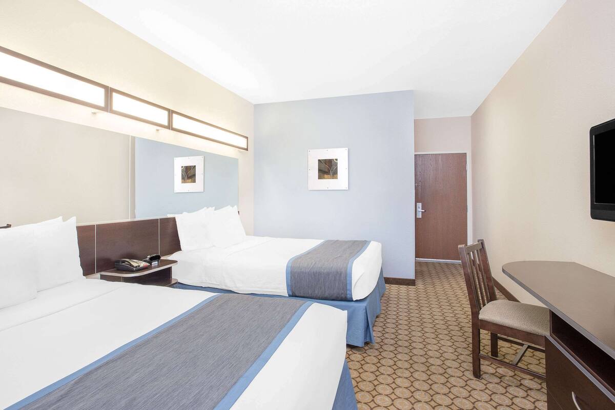 A hotel room with two beds, a desk, a chair, a television, and a door.