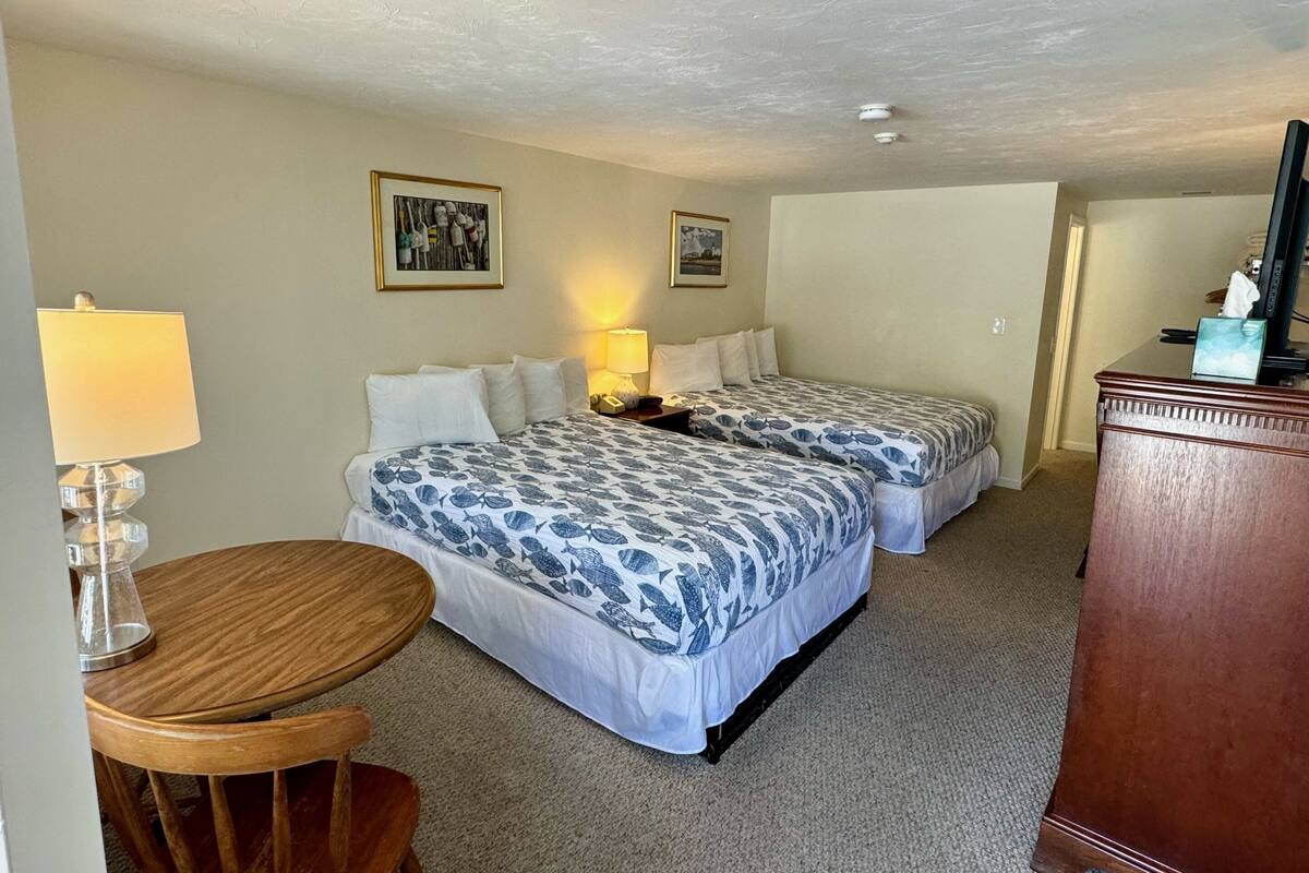 Une chambre d’hôtel avec deux lits, un bureau, une chaise, une lampe et un téléviseur.