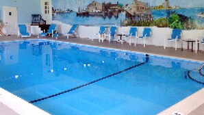 An indoor swimming pool with clear blue water, white poolside chairs, and a mural of a coastal scene on the wall. - Craigville Beach Inn (Centerville)