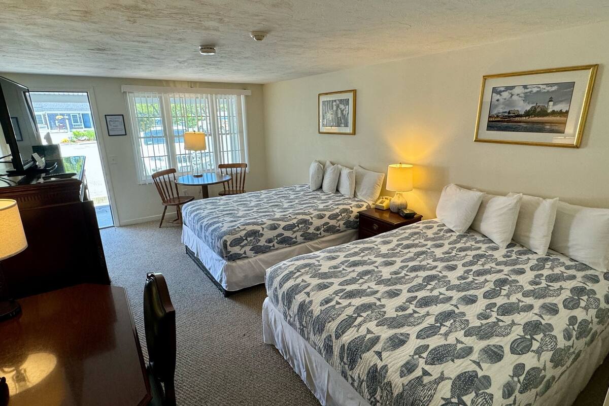 Une chambre d’hôtel avec deux lits, un bureau, une chaise, une lampe et une fenêtre donnant sur l’extérieur.