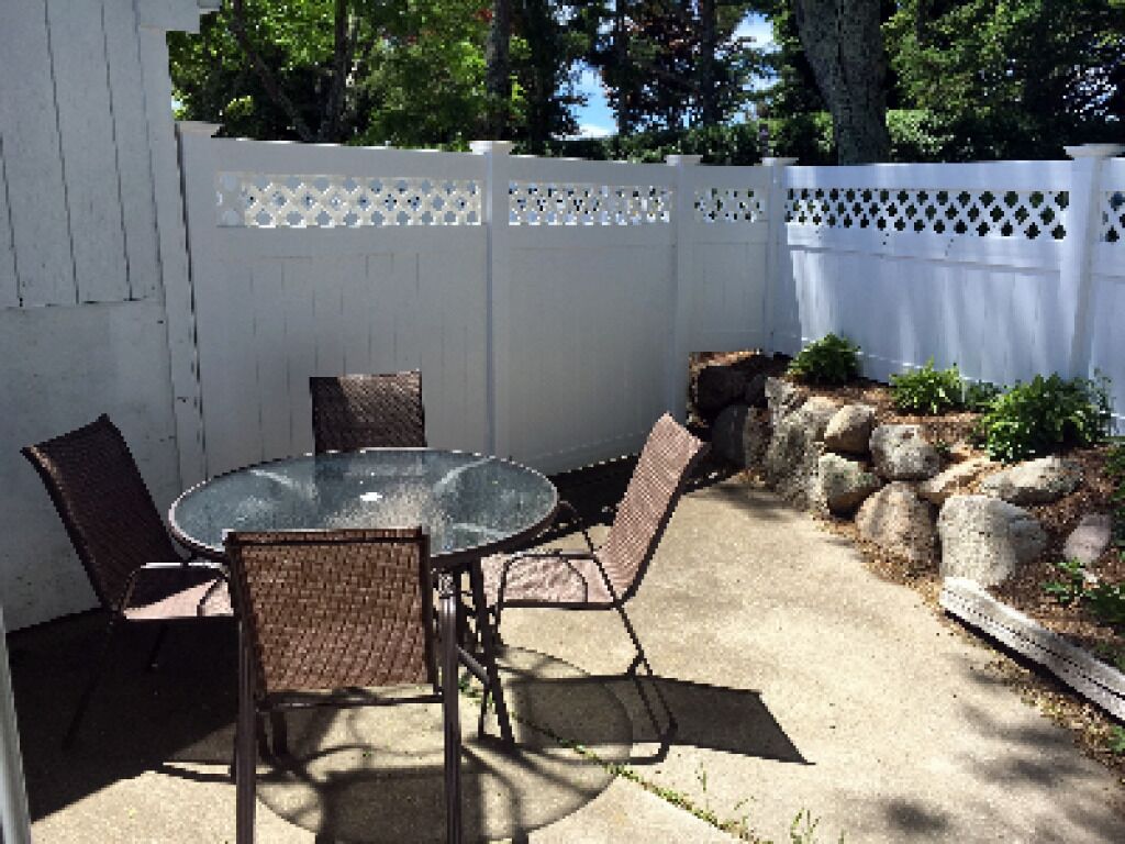 An outdoor patio with a round glass table and four wicker chairs.