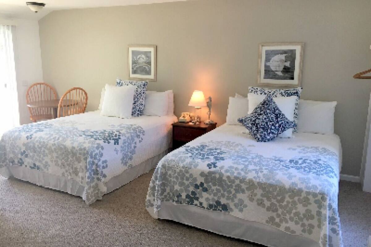 Une chambre d’hôtel avec deux lits, chacun recouvert d’une couvre-lit à motifs floraux, une table de chevet avec une lampe et deux tableaux encadrés accrochés au mur.